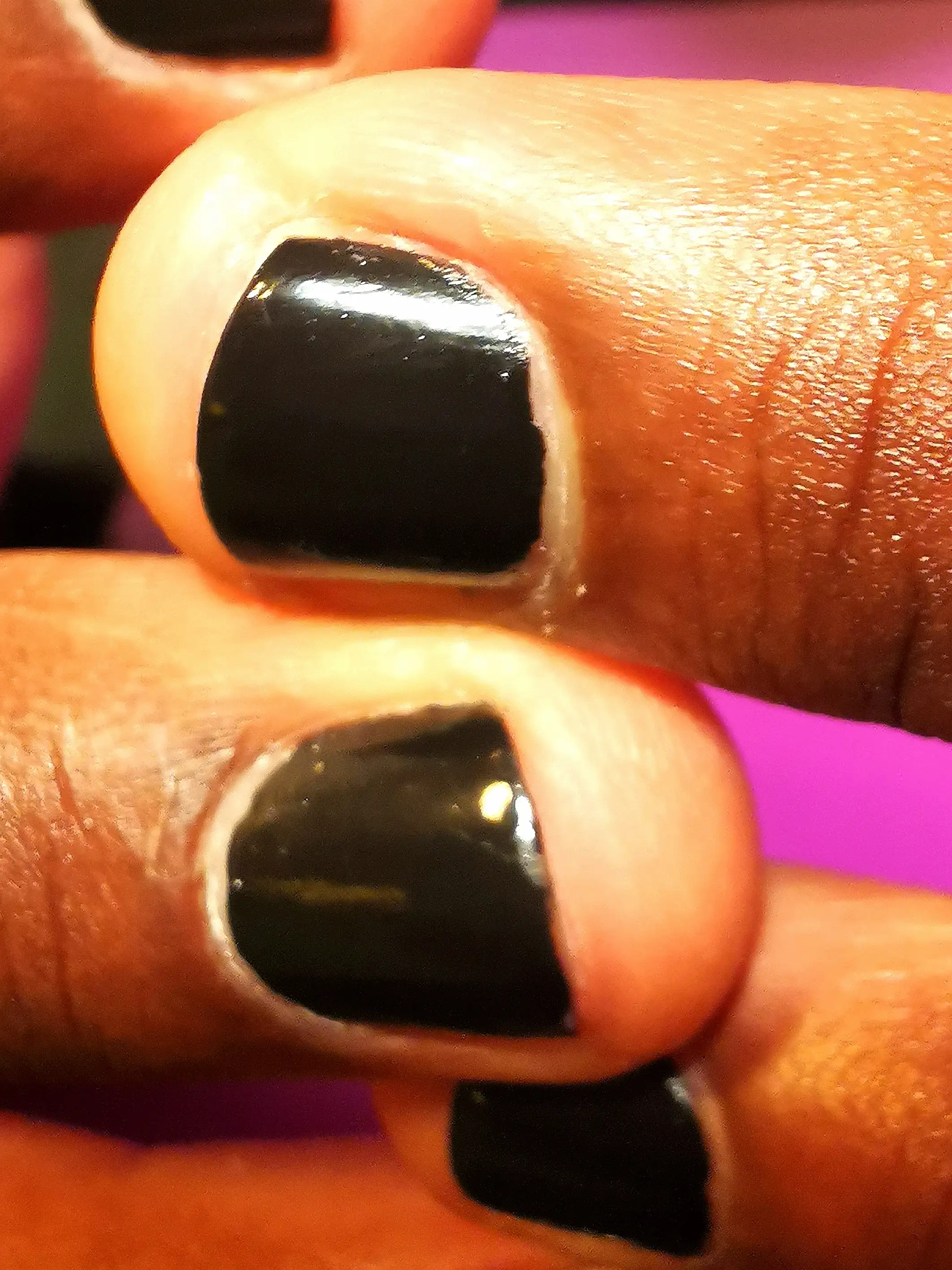 A macro shot of fingers with glossy black nail polish, emphasizing the shine and smooth finish of the nail color against the warm skin tone.