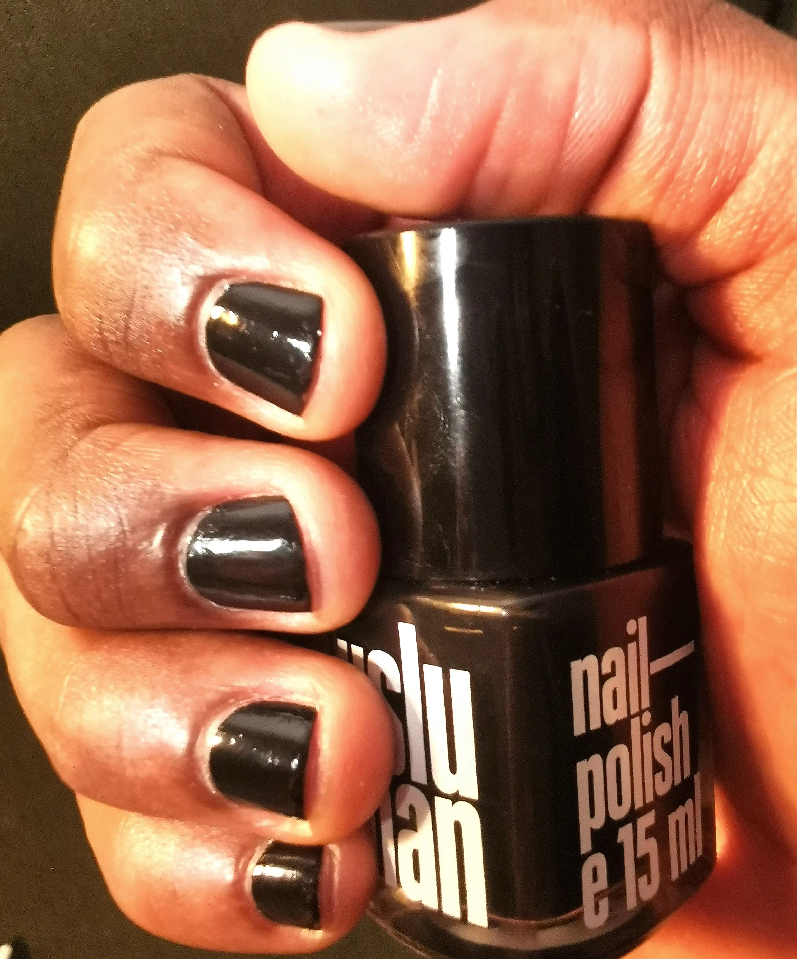 A shot of the UsluMan Nail Polish in hand with fingers with glossy black nail polish, emphasizing the shine and smooth finish of the nail color against the warm skin tone.