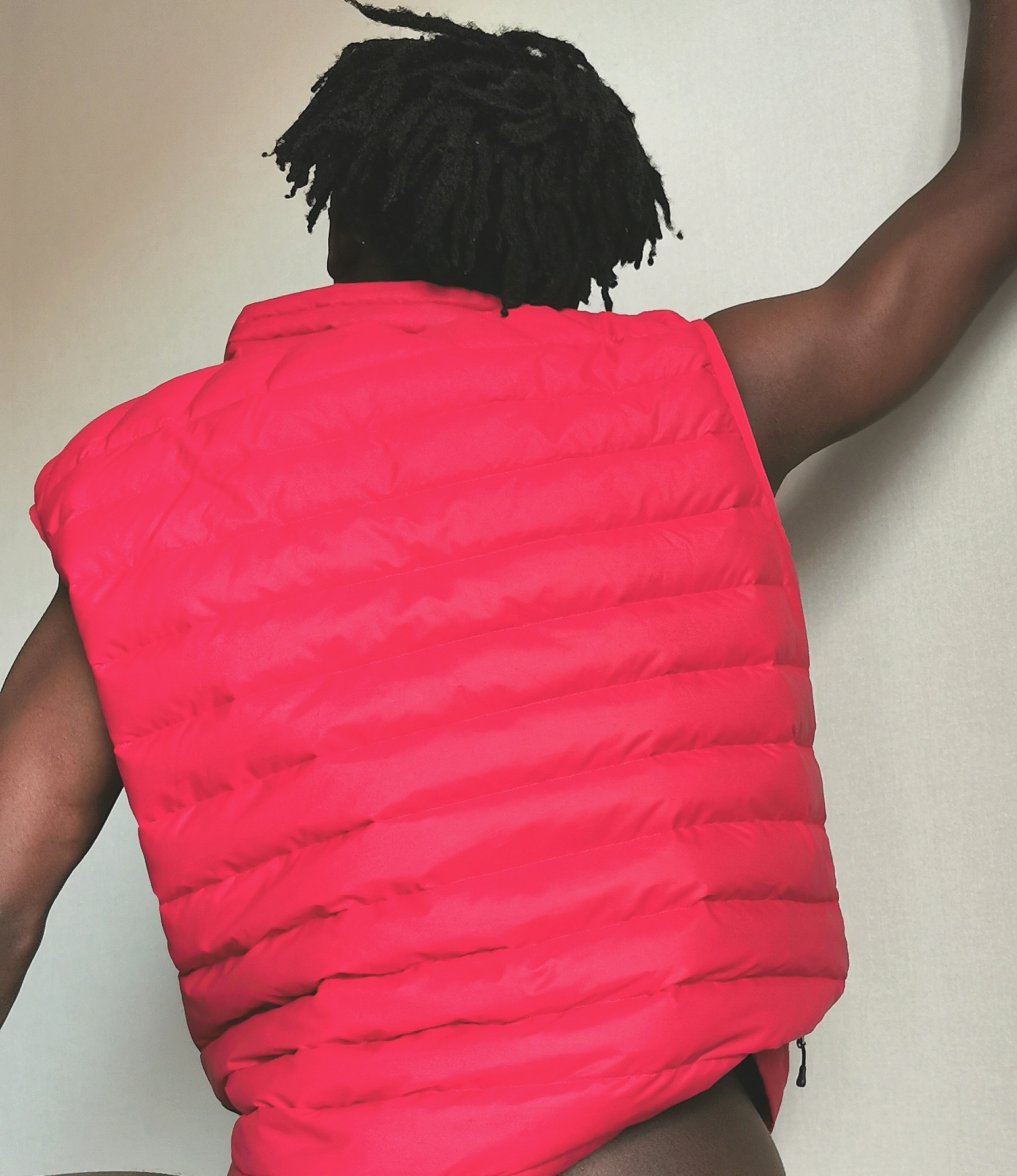 A person wearing a bright red puffer vest, photographed from behind, with their arm extended upward, showing a contrast between the vibrant vest and their dark hair.